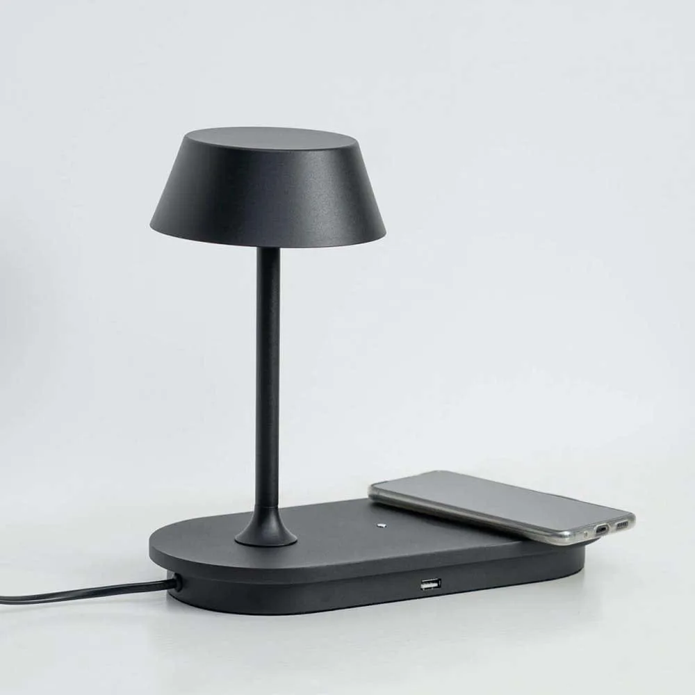 Modern matte black LED table lamp charging a phone on its wireless pad