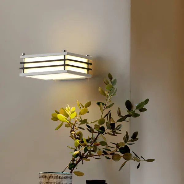 Wall sconces for bedroom: white Toast wall light glowing warm on a beige wall above a green plant