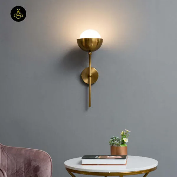 Opal white light lit on a grey wall above a round marble table with a potted plant and a pink chair