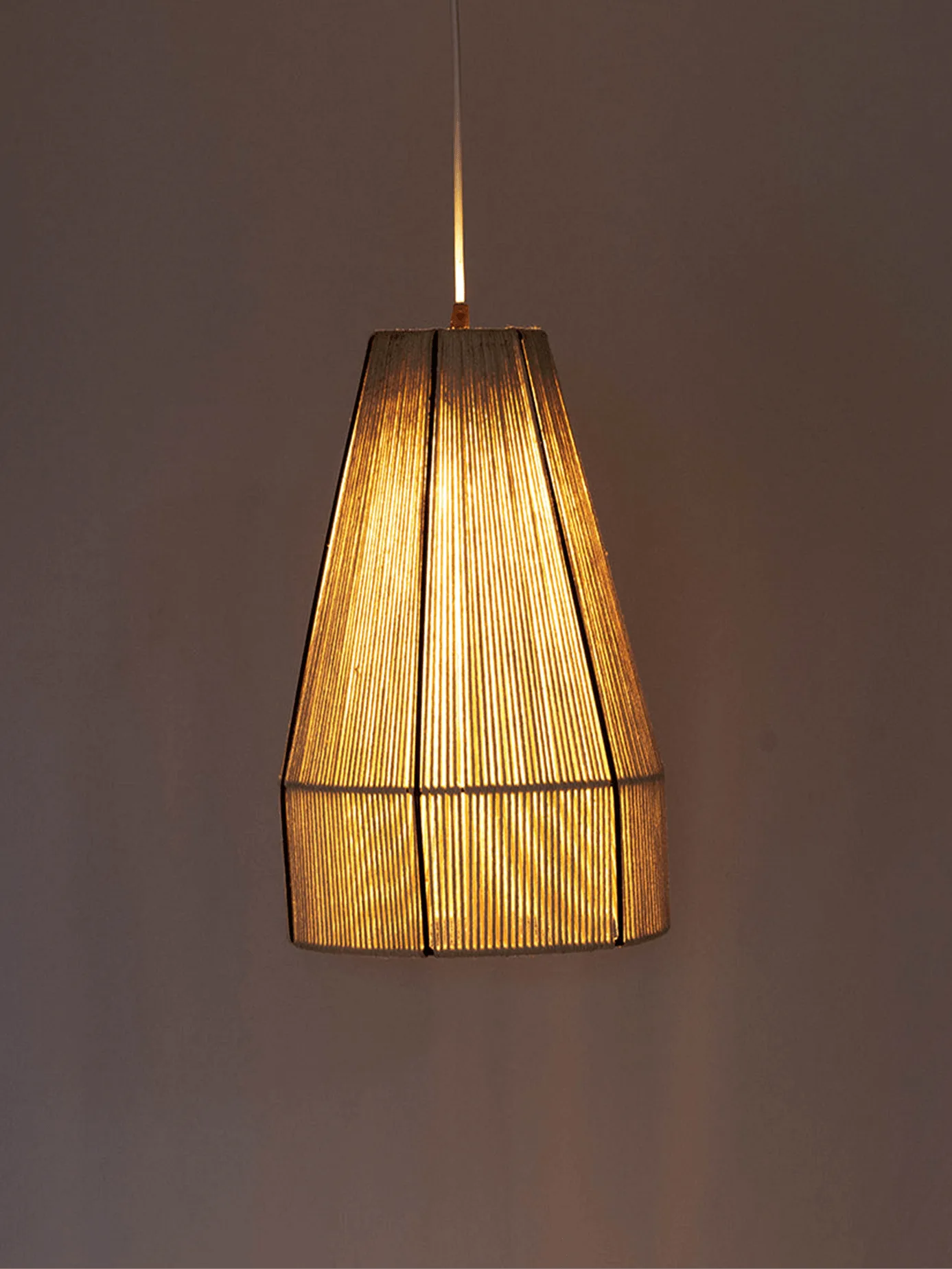 Woven Pendant Light – Handwound Raffia Cone, 16-Inch 1 Woven pendant light with natural raffia cone shade glowing warm over a grey wall