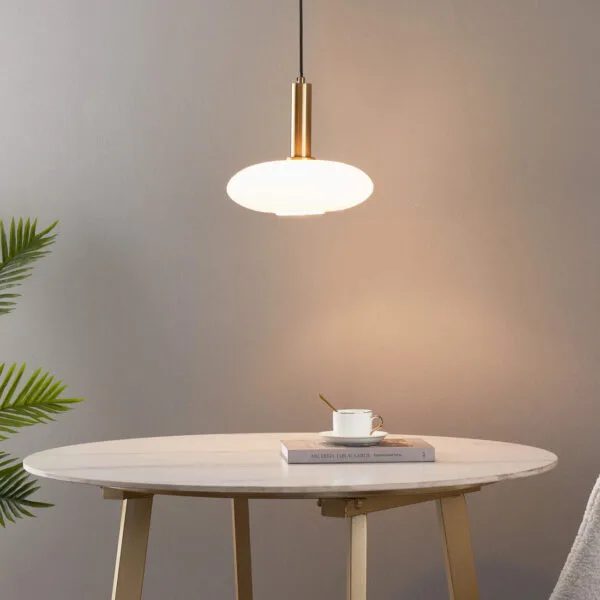 Lit opaline glass pendant light above a round marble-top table with a book and coffee cup, beside a palm plant