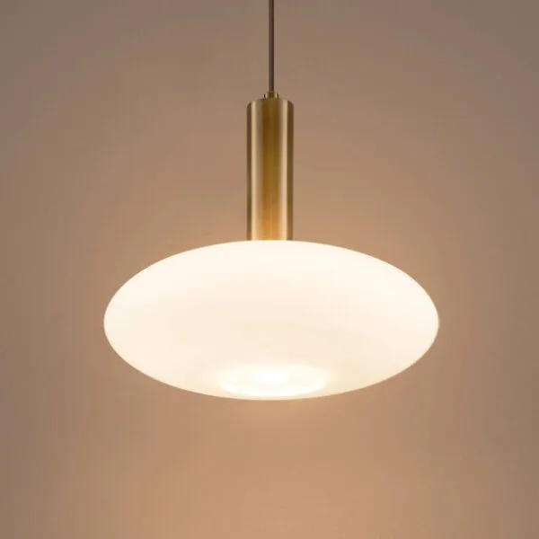Lit opaline glass pendant light, brushed gold holder above a round opal shade, against a pale wall