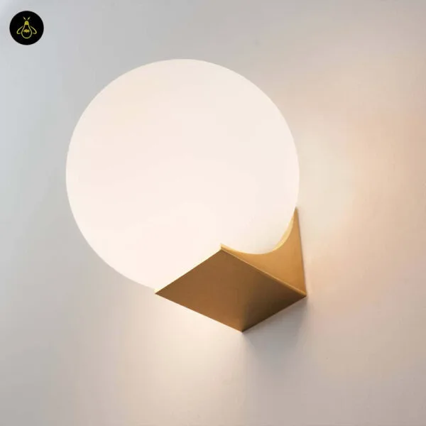 Close view of the globe wall light: opal borosilicate glass ball resting in a folded brushed-gold stainless steel base