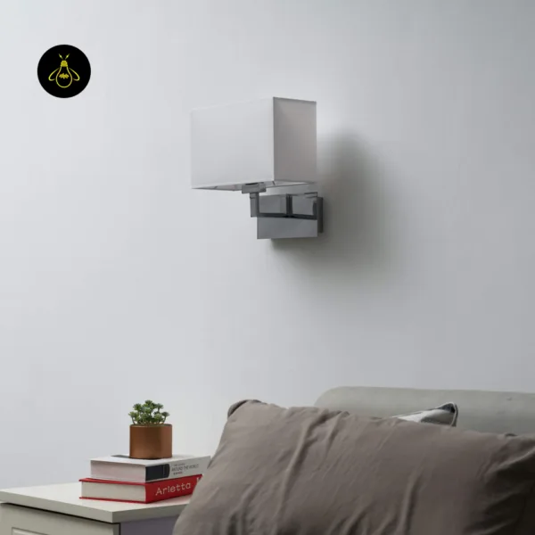 Wall lamp with shade, unlit, on a white wall above a bedside table and grey sofa