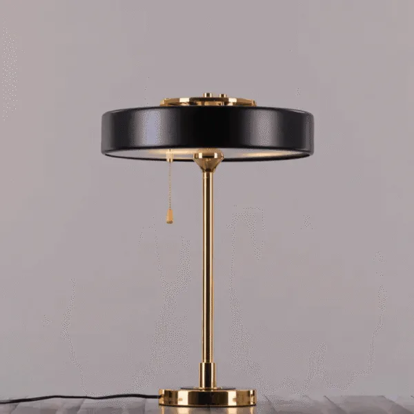 Retro study lamp on a grey backdrop with its gold stem, pull chain switch and black power cord