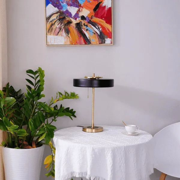 Retro study lamp on a round white table below a bright painting, with a potted plant and a tea cup