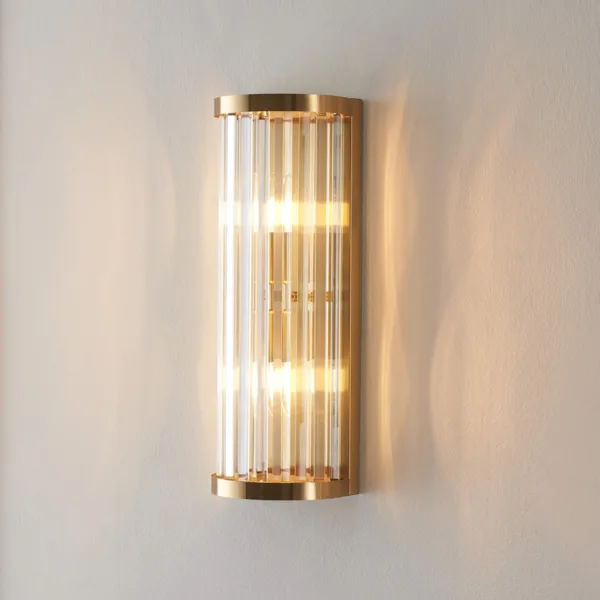 Ribbed glass wall light lit on a plain wall, clear borosilicate glass rods in a brushed gold half-cylinder frame