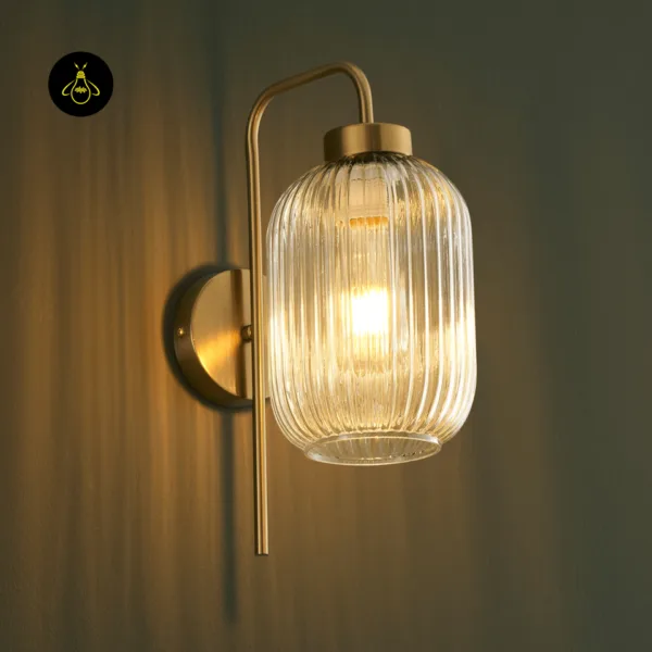 Fluted glass wall light glowing, warm light through clear ribbed borosilicate glass and a brushed gold cap