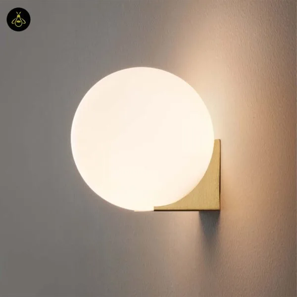 Globe wall light glowing warm white on a brushed-gold base against a grey wall
