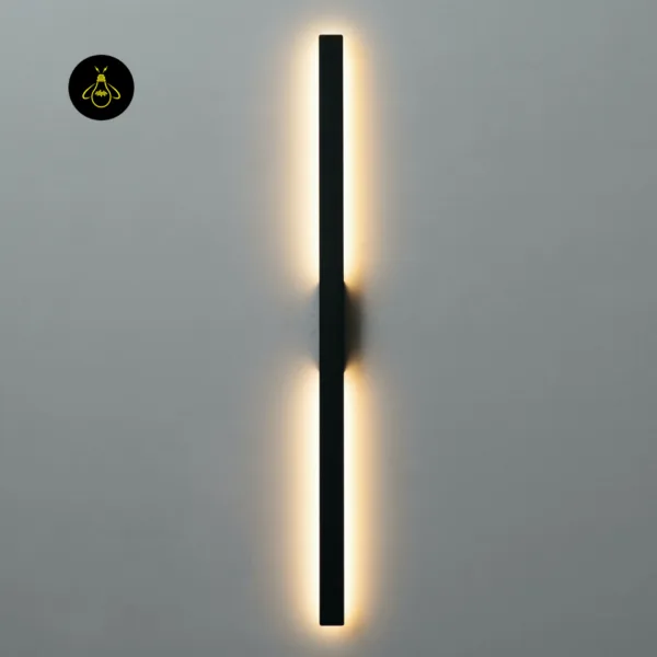 Slim LED wall light mounted vertically, warm 3000K glow running along both halves of the matte black bar on a grey wall