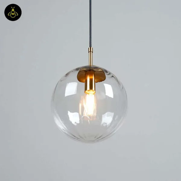 Ribbed glass ball pendant light against a grey wall, gold holder cup and lit bulb seen through the glass