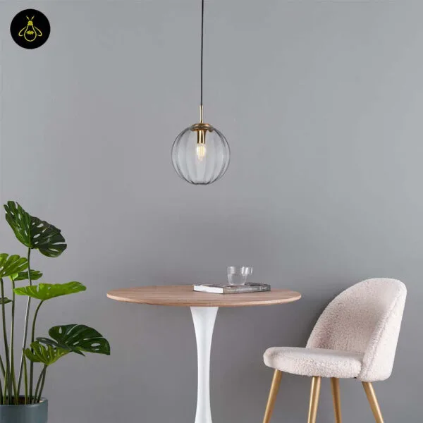 Ribbed glass ball pendant light over a round wooden dining table with a cream chair and a plant