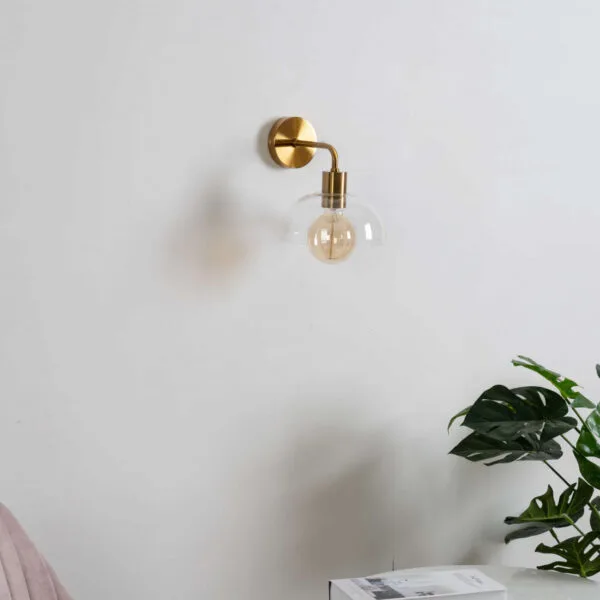 Dome wall light, unlit, on a white wall above a side table with a plant