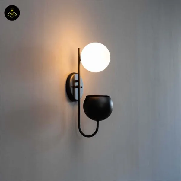Plant pot wall light lit on a grey wall, globe glowing above the matte black planter cup
