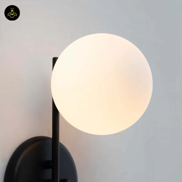Close-up of the plant pot wall light opal borosilicate glass globe lit beside the matte black backplate