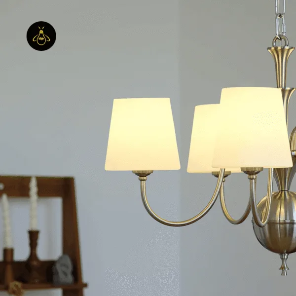 Close-up of the white chandelier lit, silk shades glowing above curved steel arms and fluted orb
