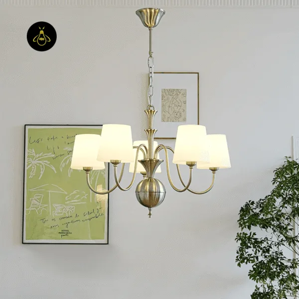 White chandelier lit warm, its five silk shades glowing beside framed art on a pale wall