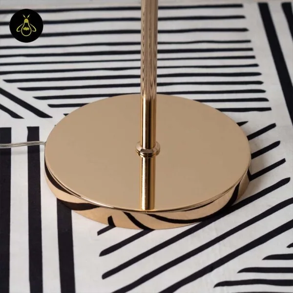 Polished gold round disc base of the white globe floor lamp resting on a striped rug