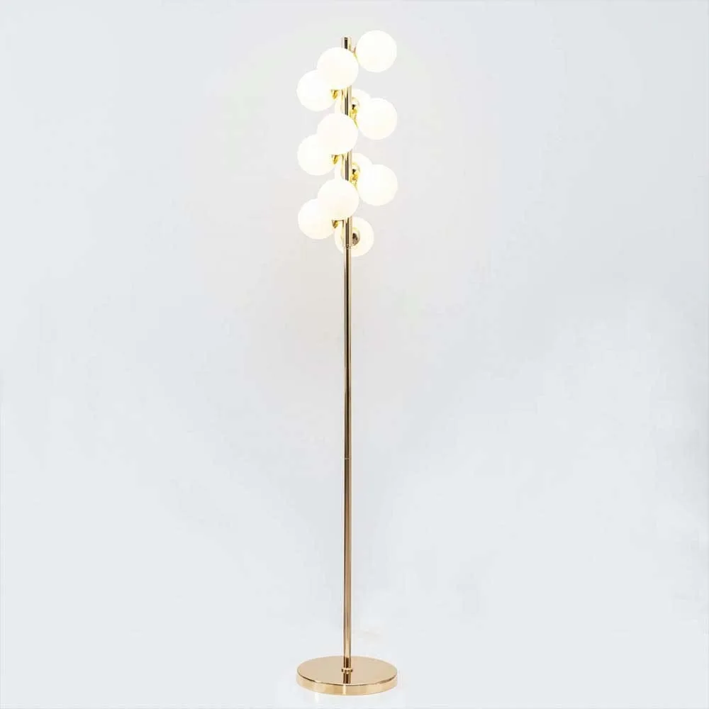 White globe floor lamp lit on a white backdrop, twelve opal glass spheres on a slim gold stand and round base