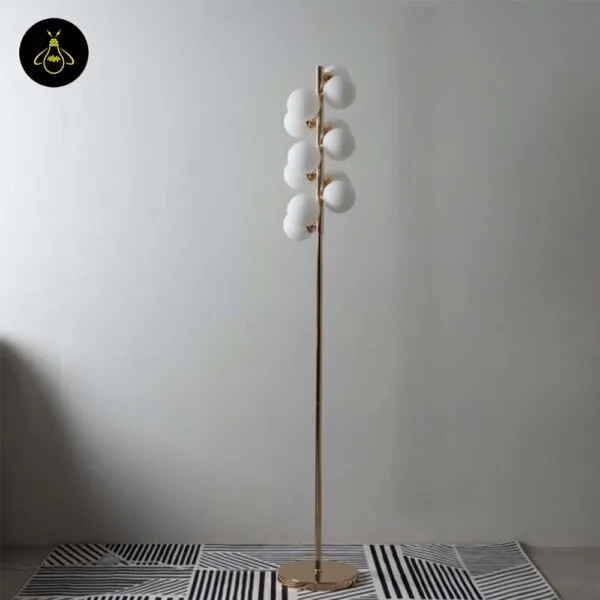 White globe floor lamp switched off, white opal spheres on a slim gold pole against a pale grey wall