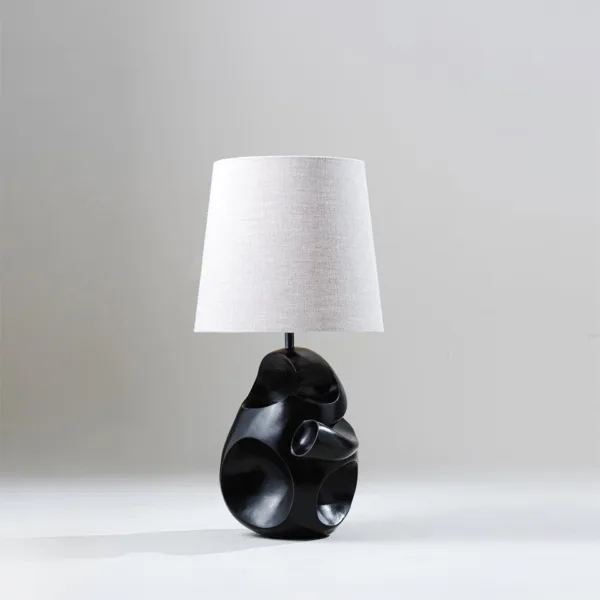 Modern table lamp with a sculptural carved charcoal-black base and natural linen shade