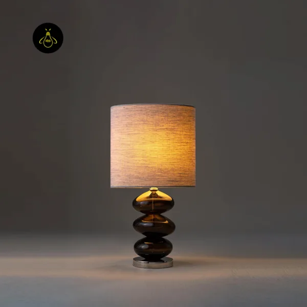 Glass table lamp glowing warm amber on a bedside surface