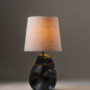 Asymmetrical table lamp lit with warm glow through linen shade