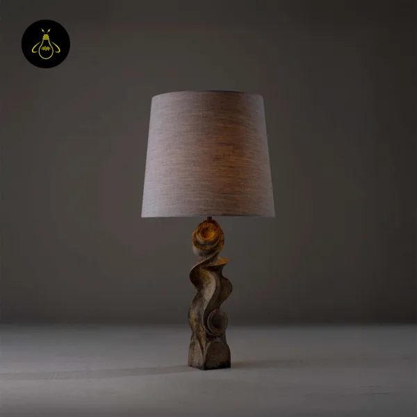 Carved wood sculptural table lamp lit with warm ambient glow through linen shade