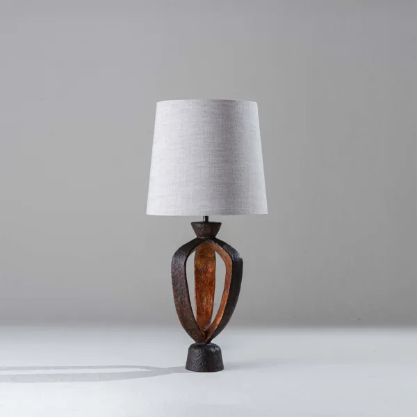 Small bedroom table lamp with a sculptural fired-copper and gold base under a natural linen shade