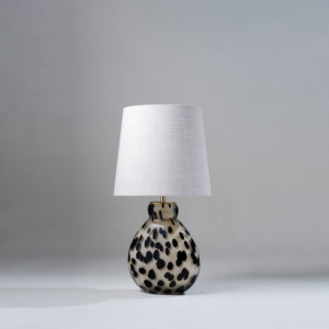 Small table lamp with spotted glass base and fabric shade on a neutral background