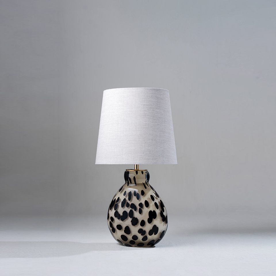Small table lamp with spotted glass base and fabric shade on a neutral background