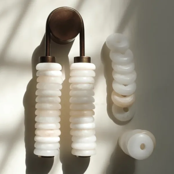 Stacked alabaster wall light beside loose white alabaster rings with centre holes, the discs that make up its columns