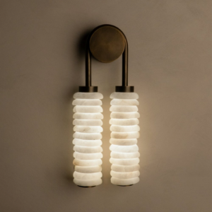 Designer wall light with double stacked alabaster drops and aged brass metal frame on a neutral wall