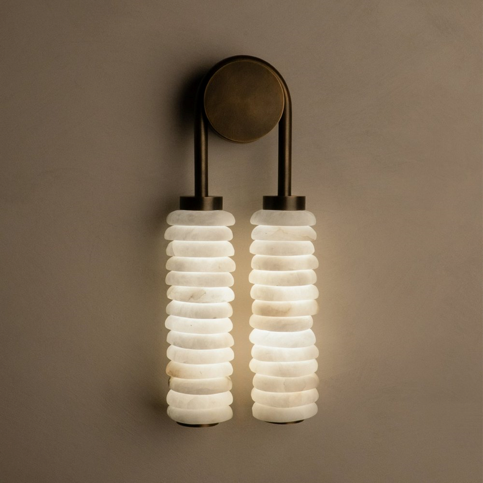 Designer wall light with double stacked alabaster drops and aged brass metal frame on a neutral wall
