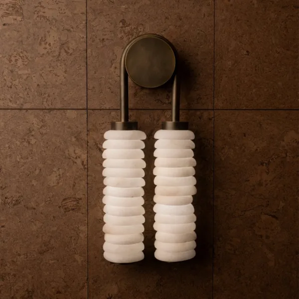 Stacked alabaster wall light on a brown stone-tile wall, twin white alabaster columns under a round aged-brass backplate