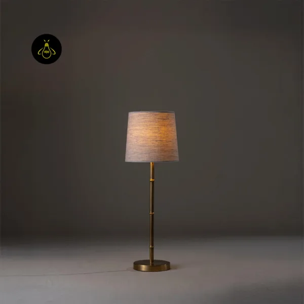 Mini brass table lamp lit to show a warm bedside glow through the linen shade