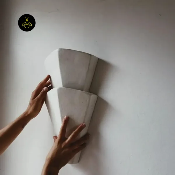 Two hands holding the tiered decorative wall light against a white wall to show its 44 cm scale
