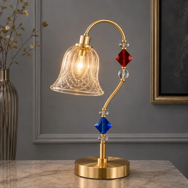 Single glass table lamp on marble surface — satin gold arc arm with diagonal-lattice cut-glass bell shade, red and blue crystal beads, warm filament glow — JagMag Lights JML-413
