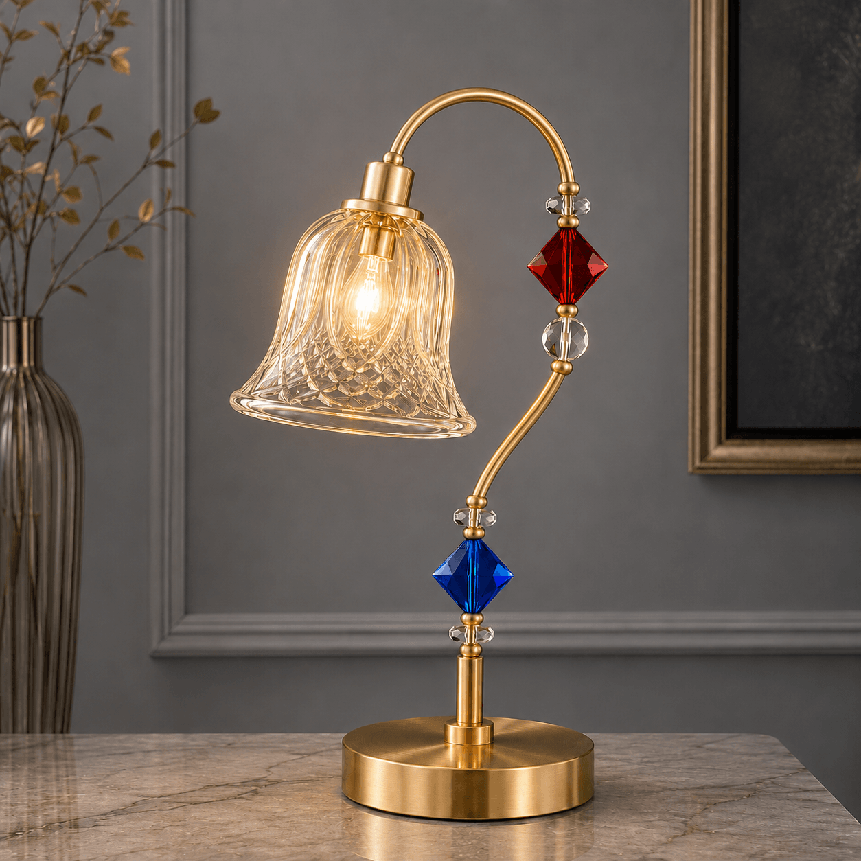 Single glass table lamp on marble surface — satin gold arc arm with diagonal-lattice cut-glass bell shade, red and blue crystal beads, warm filament glow — JagMag Lights JML-413