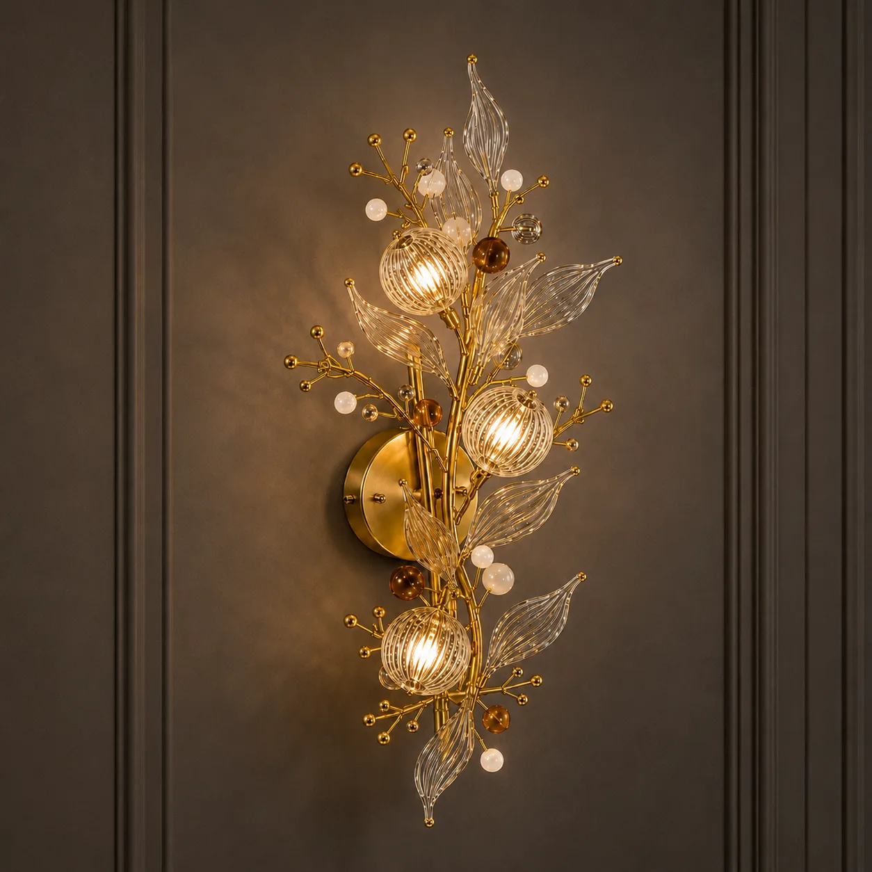 Crystal botanical wall sconce on dark paneled wall — gold branch bouquet with three ribbed glass globe shades, amber orbs and opal beads, warm filament glow — JagMag Lights JML-416