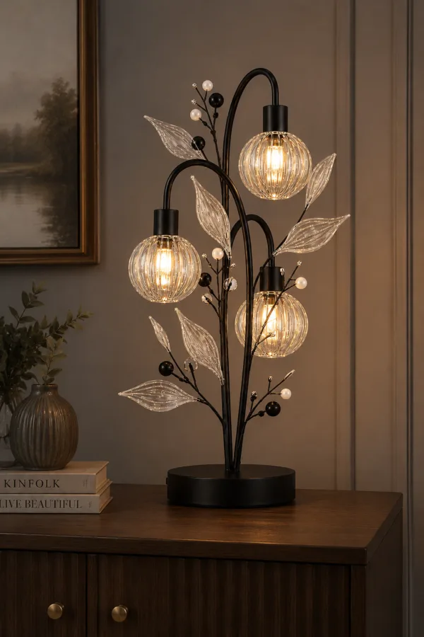 Crystal berry botanical table lamp on living room sideboard — three ribbed glass globes glowing warm amber on black branch tree, warm paneled wall setting with books and ribbed vase
