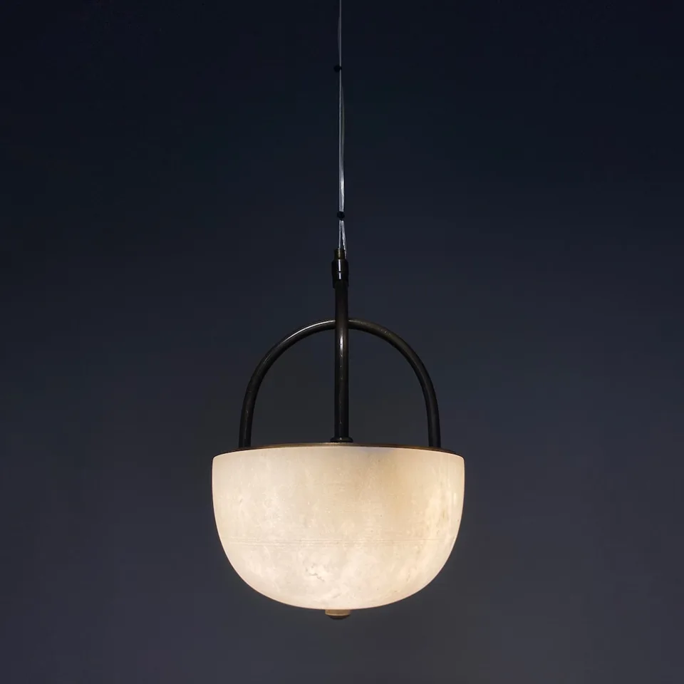 Alabaster bowl pendant light lit against a dark navy wall showing stone veining