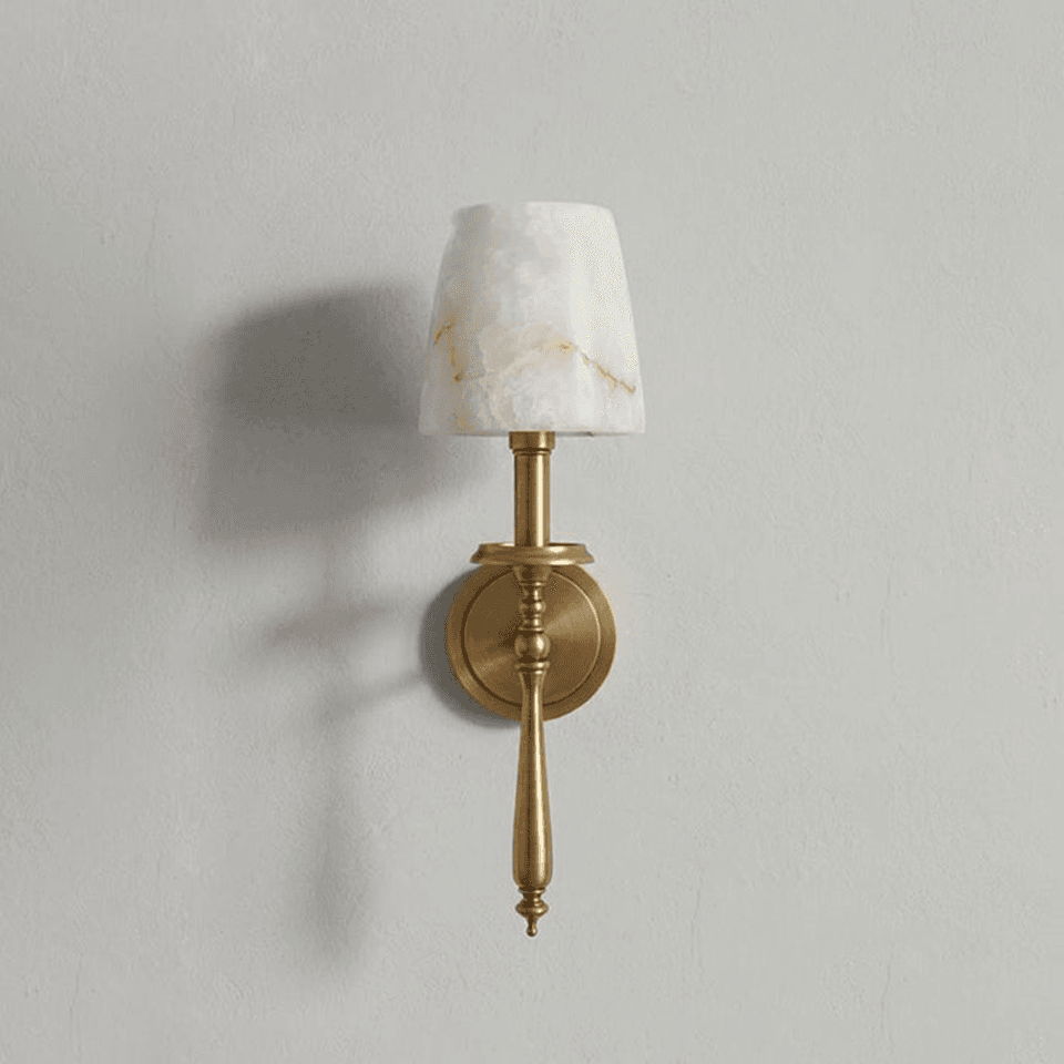 Alabaster torch wall light with a hand-cut stone shade on a turned antique brass stem