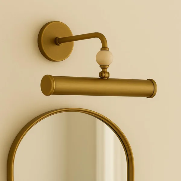 Picture wall light in antique brass finish hung above an arched mirror on a cream wall