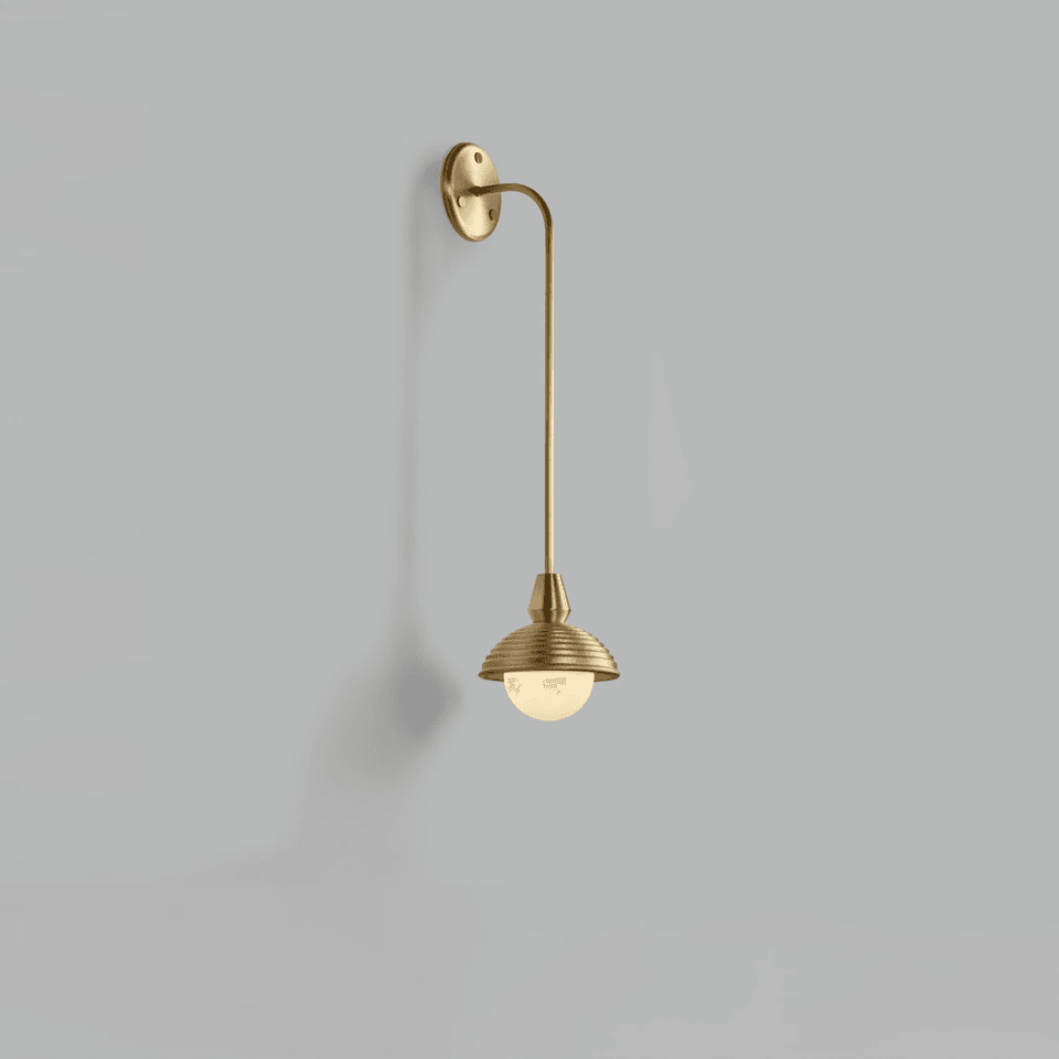 Gooseneck wall light in brushed brass, curved arm dropping to a reeded dome shade with an opal glass ball, on a grey wall