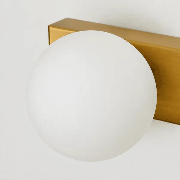 Close-up of the opal borosilicate glass globe of the green wall light on its brushed brass finish plate
