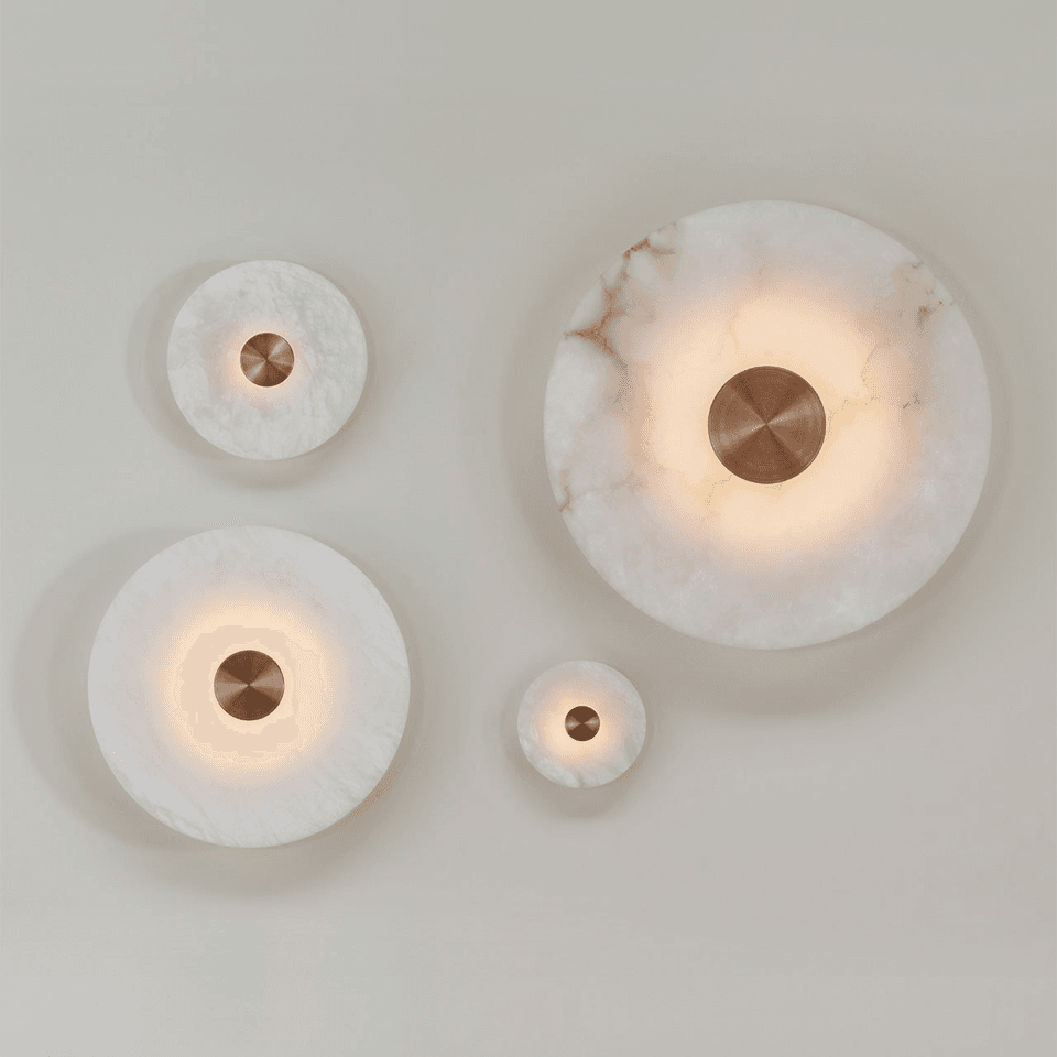 Four sizes of the Alabaster Eclipse disc wall light lit together on a wall, from ø180 mm up to ø625 mm, each with a brushed bronze centre