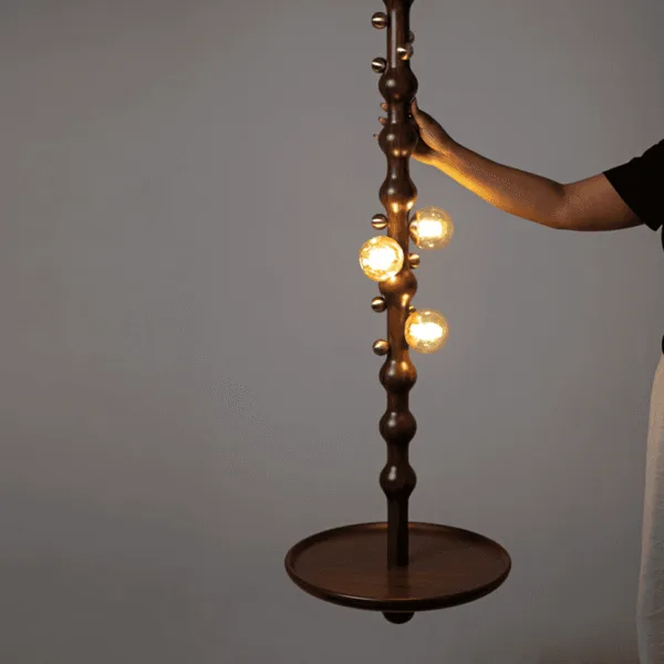 Person holding the turned stem of the lit teak wooden hanging lamp, showing its scale