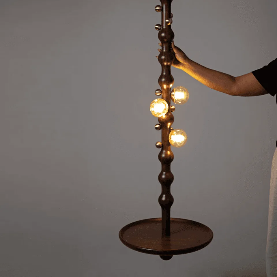 Stem Pendant Light – Sculpted Reclaimed Teak with Amber Glass Globes & Side Table | Jagmag Lights 6 Person holding the Stem pendant light stem, showing the scale of the tall sculptural pendant