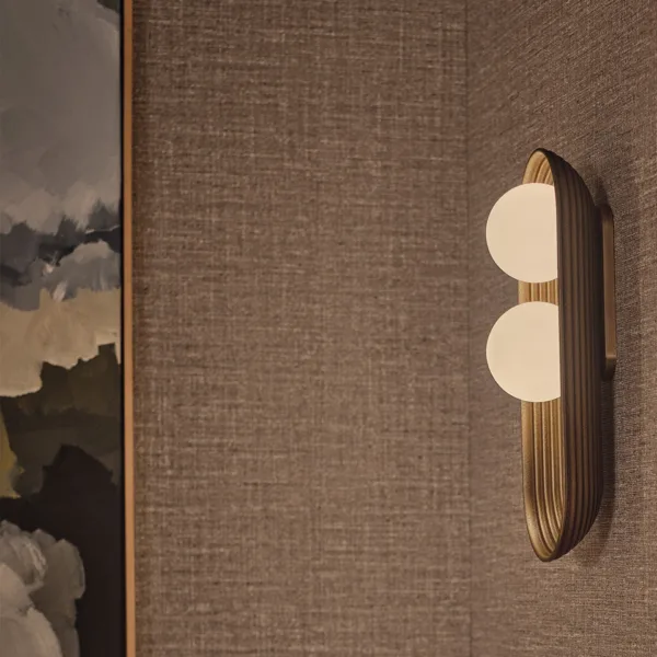Matt-gold twin oval wall light mounted on a textured grasscloth wall beside framed artwork